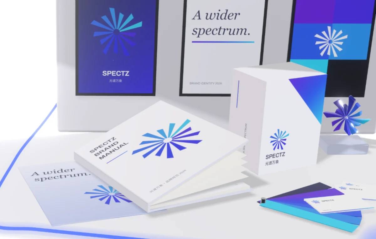 浮在空中翻开的 SPECTZ 品牌手册、印着星芒标志的产品盒、一把色卡扇与名片，后方是品牌海报墙